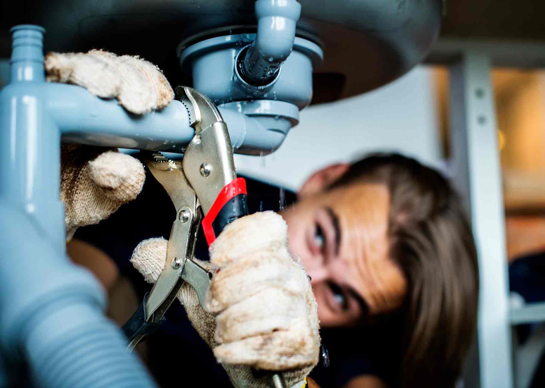 A plumber using a wrench to fix a clogged kitchen sink pipe, highlighting the importance of maintaining clear drains.